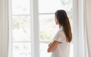 brunette woman looking out window with arms crossed