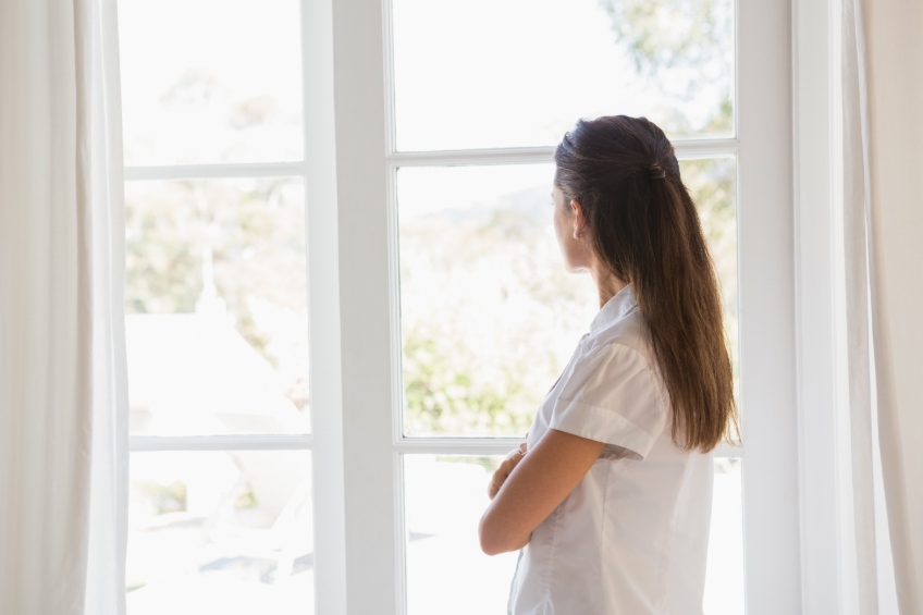 brunette woman looking out window with arms crossed